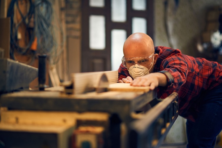 Man with carpenter's insurance sawing a piece of wood