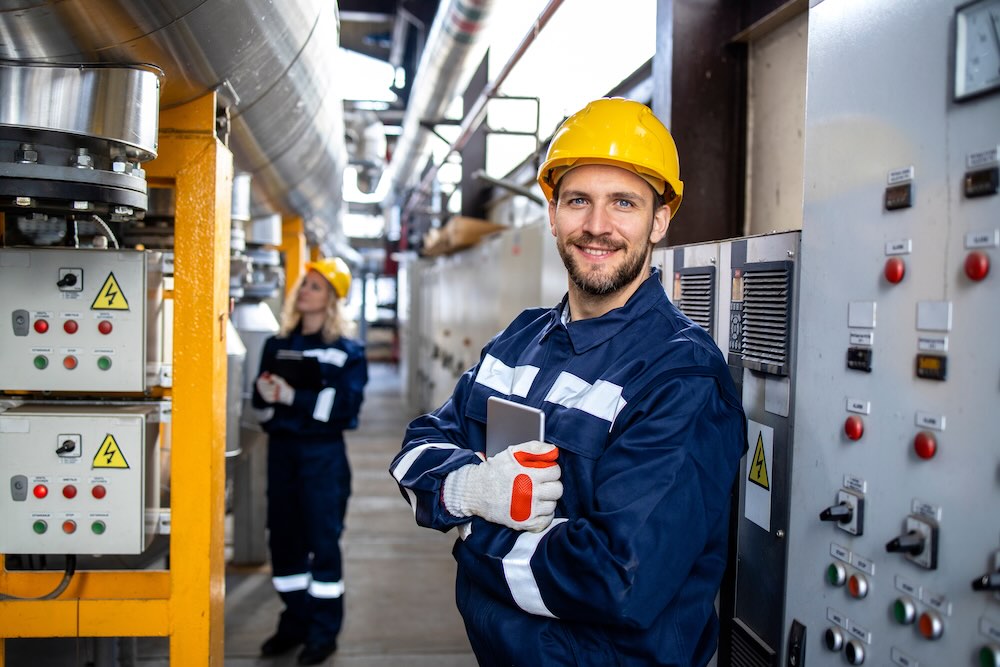 Man with electricians insurance smiling in front of machinery