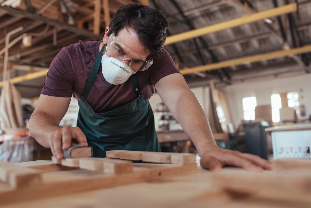 Man with general property insurance sanding down a piece of wood