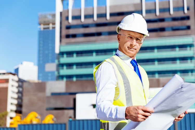 Man with engineers insuarance holidng plans and wearing a hardhat