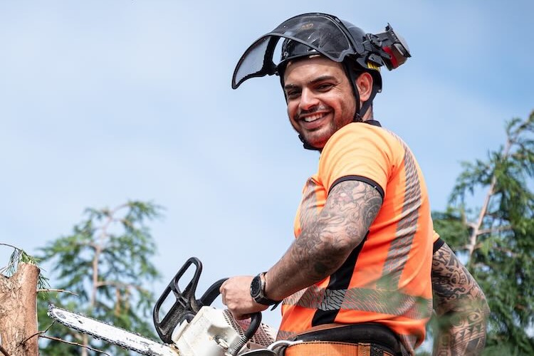 Male contractor with arborist insurance chopping tree branches with a chainsaw